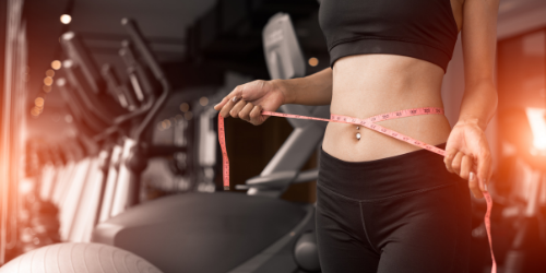woman at the gym in workout clothes with measuring tape around her waist